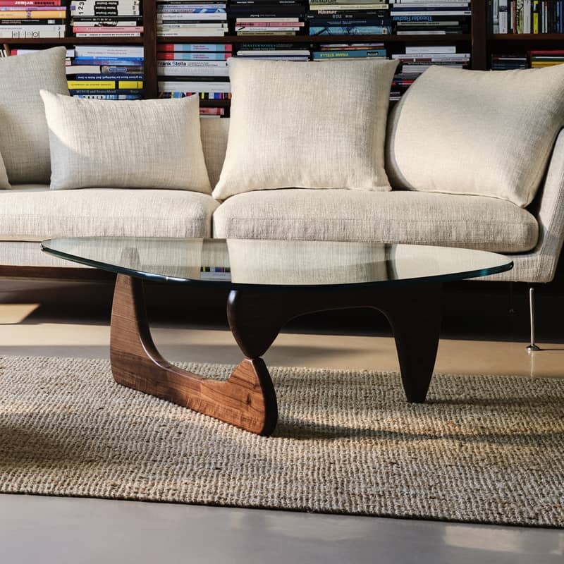 Ein Couchtisch mit Glasplatte und kunstvoll geschwungenen Holzbeinen steht im Wohnzimmer vor einem Sofa